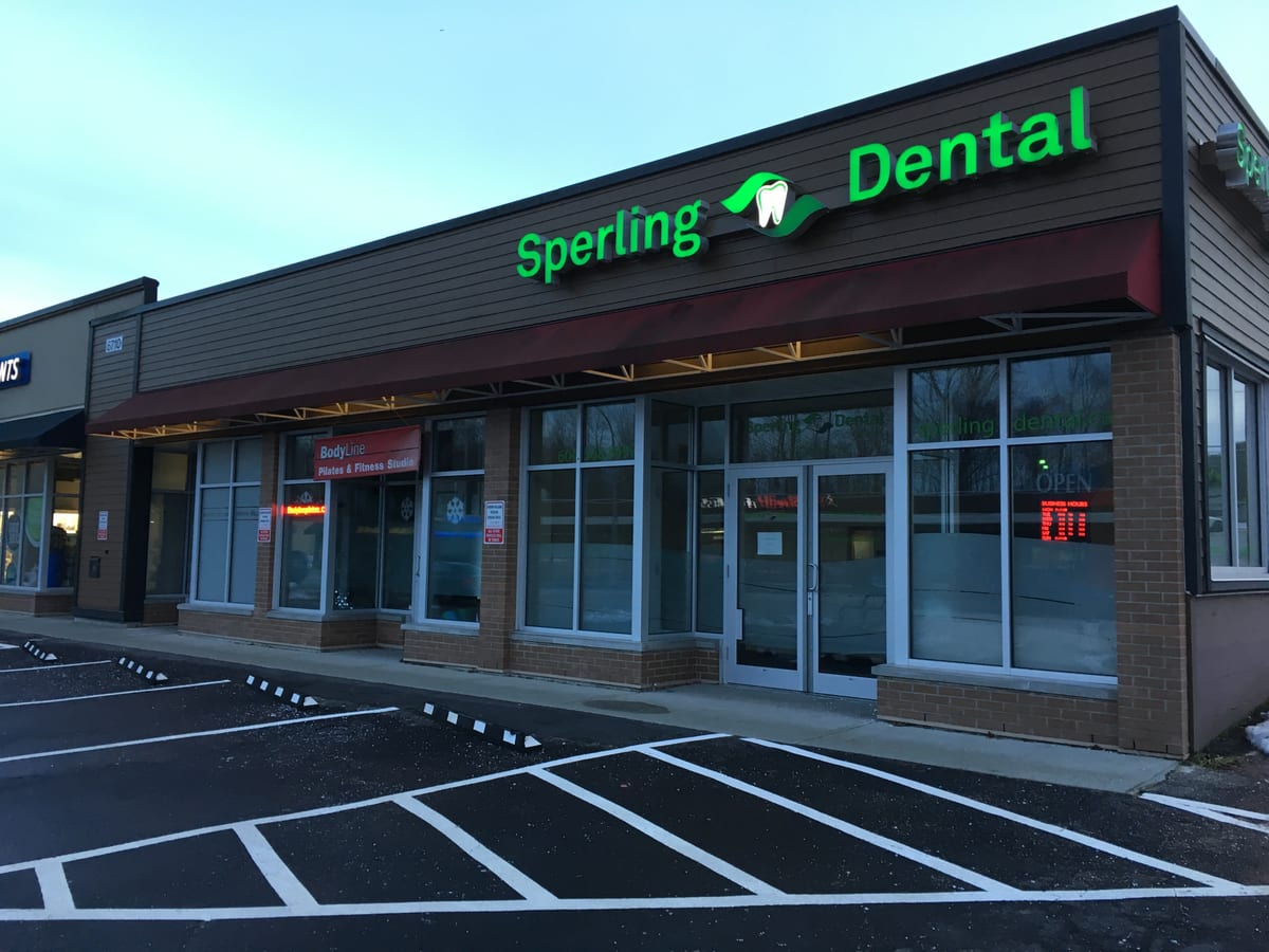 The Sperling Dental storefront at dusk, with its lit green sign above the entrance